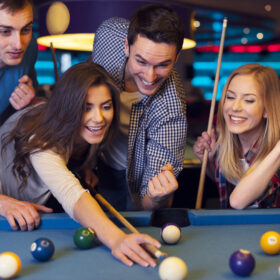 Friends cheering while their friend aiming for billiards ball